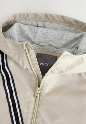 Lichtbeige ritsjack met een grijze capuchonvoering, voorzien van een opvallende zwart-witte gestreepte accent. De ritssluiting heeft een sterdetail.