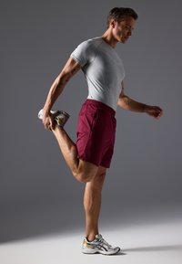 Αθλητική ενδυμασία που περιλαμβάνει ένα γκρι κοντομάνικο μπλουζάκι, μπορντώ κοντές βερμούδες με τσέπες και γκρι αθλητικά παπούτσια τρεξίματος με μεταλλικές λεπτομέρειες.