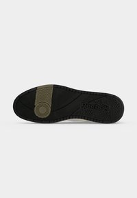 Πάτος ενός μαύρου και ελιάς παπουτσιού Reebok με υφασμένα σχέδια και το λογότυπο Reebok στην περιοχή της φτέρνας.