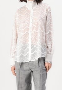 White sheer blouse with a wavy embroidered pattern and buttons, featuring long sleeves and lace accents at the collar and cuffs.