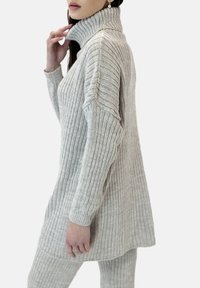 Maglione a coste di un grigio chiaro, con collo alto, dal fit rilassato e maniche lunghe. Texture morbida e silhouette allungata.
