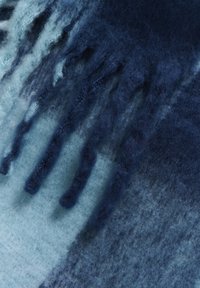 Blødt uldtørklæde med gradientnuancer af blå og en tekstureret finish. Flosset kant og subtile farvevariationer giver dybde.