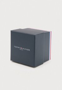 Dark blue Tommy Hilfiger watch box with logo and red, white, and blue stripe detail on a light background.