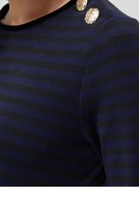 Granatowa i czarna bluzka w paski z okrągłym dekoltem, z trzema złotymi guzikami na ramieniu. Miękki materiał o gładkiej fakturze.