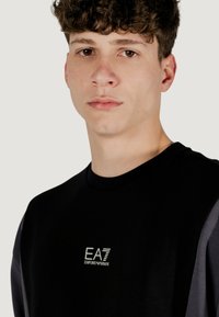 Felpa nera con logo sul petto e accenti grigi sulle maniche. Il tessuto appare liscio e aderente.