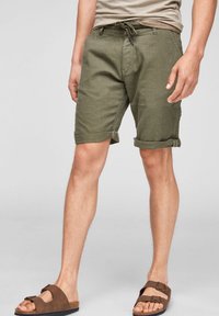 Shorts en lin vert olive avec revers roulés, dotés d'une taille à cordon et de poches latérales, assortis à des sandales marron.