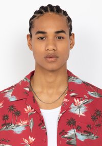 Rode shirt met korte mouwen in een tropisch bloem- en palmboompatroon, met een ingesneden kraag en knoopsluiting aan de voorkant, gedragen over een wit T-shirt.