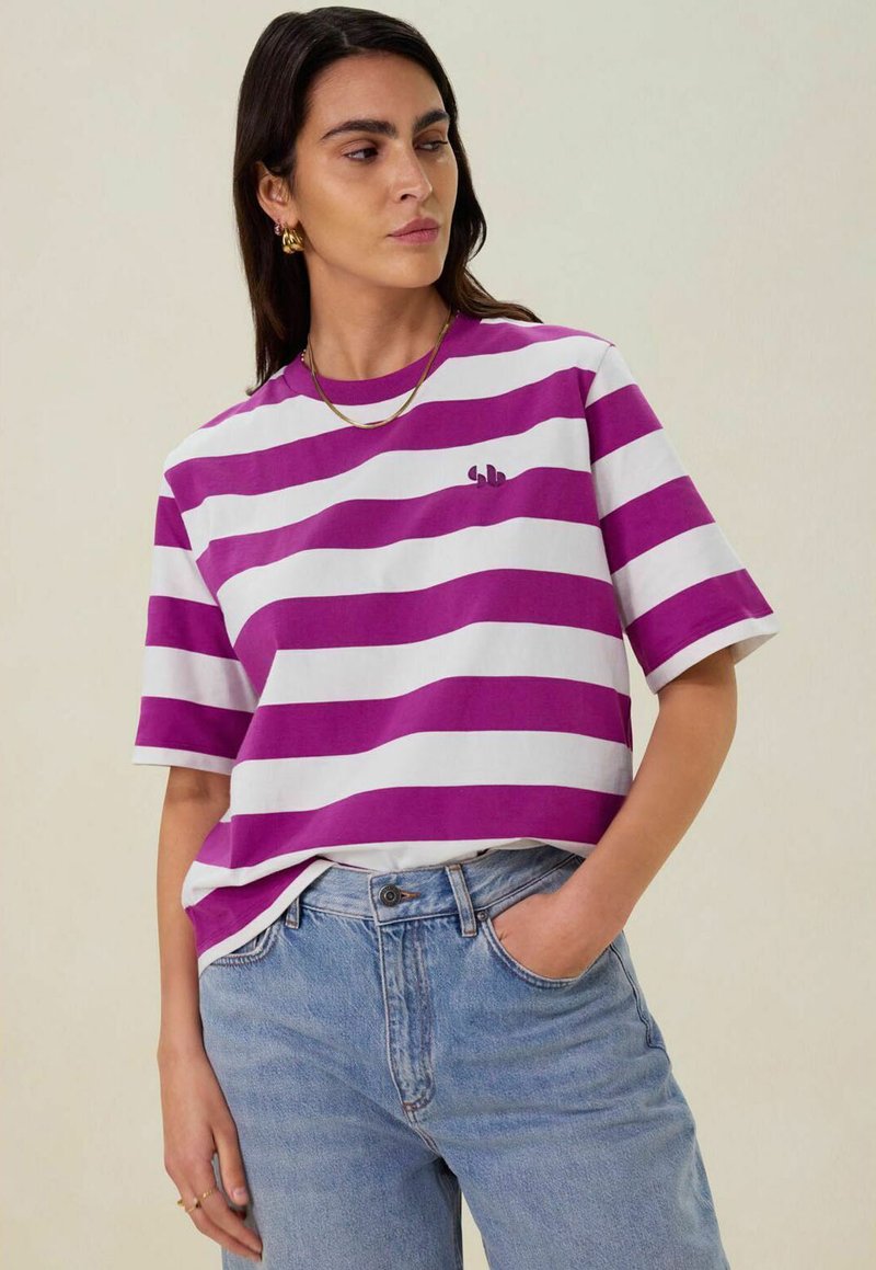 Korte mouwen, cropped t-shirt met paarse en witte horizontale strepen. Heeft een klein logo op de borst en een losse pasvorm.