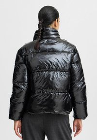 Veste matelassée noire avec une finition brillante, col montant et motif couturé horizontal. Présente une silhouette courte et des poignets élastiques.