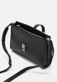Sort læder håndtaske med rektangulær form, sølv hardware, lynlås lukning og justerbar rem. Glat tekstur med minimalistisk design.