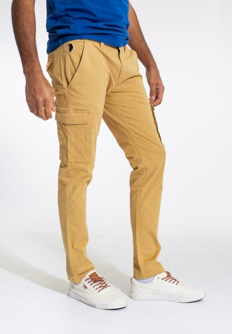 Beiga cargo byxor med fickor, slim fit, gjorda av slitstark bomullstyg. Matchas med vita sneakers och en blå topp.