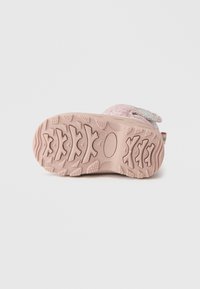 Ροζ παιδικά παπούτσια με υφασμάτινη σόλα από καουτσούκ με ανάγλυφο σχέδιο κυματισμού και στρογγυλές τάπες, στερεωμένα με λουράκι με αυτοκόλλητο στο πλάι.