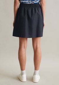 Donkerblauwe rok met een elastische smock tailleband, gestructureerde silhouette, boven de knie lengte, gecombineerd met witte sneakers en sokken.