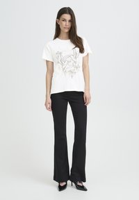 Cotton T-shirt in off-white with a printed design featuring birds and flowers. Paired with black flared pants and pointed toe heels.