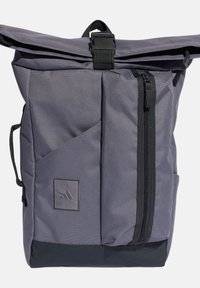 Šedý nylonový batoh s rolovacím designem, vybavený přední kapsou na zip, texturovanou tkaninou a značkovou etiketou blízko spodní části.