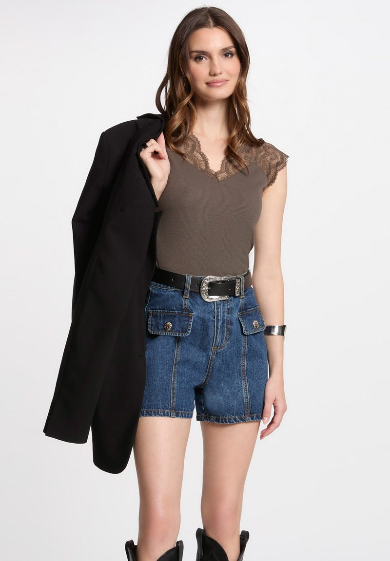 Braunes geripptes Tanktop mit Spitzenbesatz, kombiniert mit hochtaillierten blauen Jeansshorts mit Fronttaschen, und einem schwarzen Blazer über der Schulter.