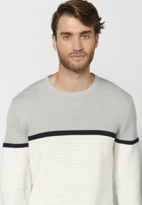Maglione lavorato a maglia grigio e bianco sporco con un motivo a coste orizzontali, caratterizzato da una sezione grigia uniforme e un accento nero vicino al colletto.