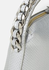 Stříbrná kabelka s texturou v podobě šupin. Má lesklé kovové držadlo a zlatý zip pro uzavření.