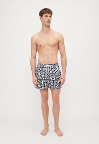 Schwarze und weiße gemusterte Badeshorts mit elastischem Bund und Kordelzug. Verfügt über ein florales und abstraktes Design.