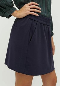 Jupe bleue marine en tissu doux, dotée d'une taille élastique, d'une poche latérale et d'une coupe décontractée avec un design simple.