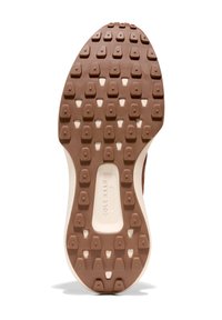 Skosula har en brun gummiyta med hexagonala mönster och vita accenter. Märkesnamnet "Cole Haan" syns i mitten.