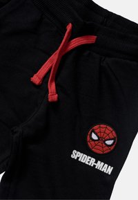 Black pants with red drawstring and embroidered red Spider-Man face logo above white "SPIDER-MAN" text on the right leg.