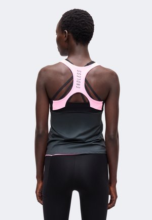 Kobieta ubrana w czarne legginsy sportowe i czarny top z różowym sportowym biustonoszem typu racerback, na którym na plecach jest napisane "ENDLESS".