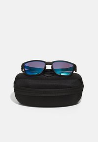 Juodos saulės akinių su atspindinčiais mėlynais lęšiais, turinčiais stačiakampį rėmelį. Komplekte yra juodas tekstūruotas kietas dėklas su užtrauktuku.