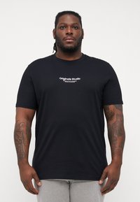 Sort bomulds t-shirt med korte ærmer og rund halsudskæring. Har et hvidt trykt logo "Originals Studio" på tværs af brystet.