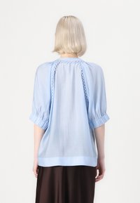 Lichtblauwe blouse met korte, opgezette mouwen, voorzien van een decoratieve kantafwerking langs de achterkant van de yoke; gemaakt van een zachte, lichte stof.