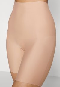 Beige høyt liv shaping shorts laget av glatt, elastisk materiale. Har et rent, sømløst design med minimal søm.