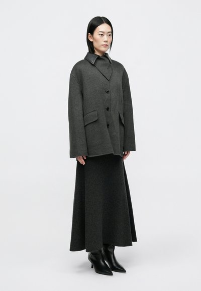 Pilkas didelio dydžio paltas su apykakle, priekyje mygtukų uždarymas ir šoniniai kišeniai. Sujungtas su ilgu pilku sijonu ir juodais smailiais auliniais batais.