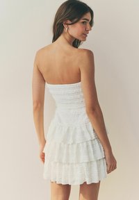 Vit strapless klänning med en åtsittande bodice och tre lager volanger vid kjolen. Texturen har ett subtilt randigt mönster.