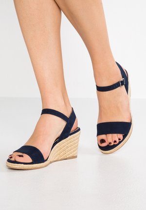 Navy suede wedge sandals with a textured jute heel, featuring a wide front strap and an ankle strap with a buckle closure.