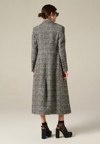 Cappotto lungo a scacchi bianco e nero con vestibilità su misura e colletto a successivo. Presenta maniche lunghe, fessure laterali e dettagli di cucitura decorativi.