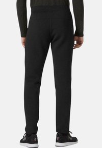 Pantalones de chándal negros con una textura suave, ajuste ajustado, cintura elástica y bolsillos, combinados con zapatillas negras que tienen un acento de logo.