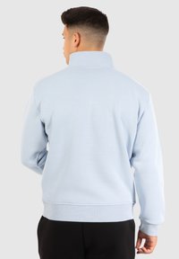 Pull léger bleu avec un col montant, des poignets et un ourlet côtelés. Sa texture douce et son design simple offrent une coupe décontractée et confortable.