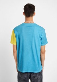 Camiseta de corte holgado con un cuerpo azul y mangas cortas amarillas. Fabricada en algodón, cuenta con cuello redondo y una textura suave.