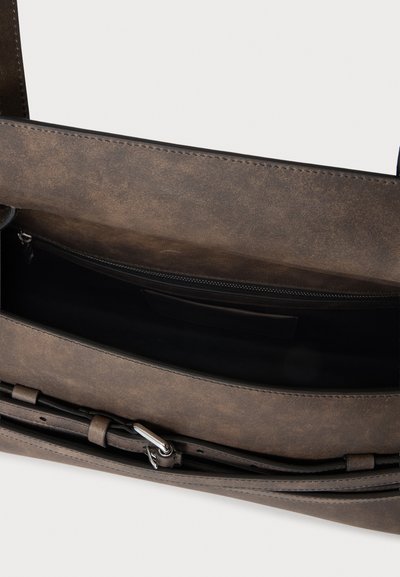Sac en cuir marron ouvert montrant un compartiment intérieur avec une poche zippée et une sangle réglable avec boucle argentée.