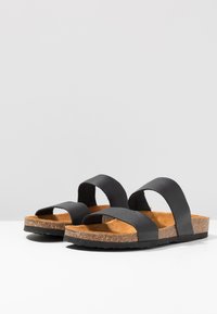 Sandali in pelle nera con due ampie cinghie, suola in sughero e suola in gomma testurizzata. Design minimalista con silhouette piatta.