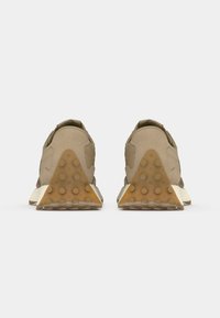 Beige joggesko med teksturert overdel, triangulær beige hæl og gummisåle med sirkulære gripe mønstre. Enkelt design med minimale detaljer.