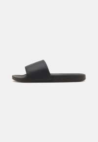 Sandale noire à semelle plate avec une bride texturée et un design minimal. Fabriquée en matériau synthétique, avec un détail de logo subtil.