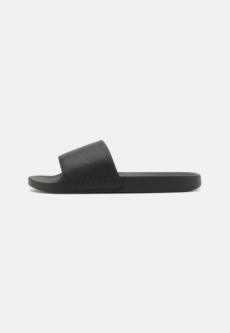 Sandale noire à semelle plate avec une bride texturée et un design minimal. Fabriquée en matériau synthétique, avec un détail de logo subtil.