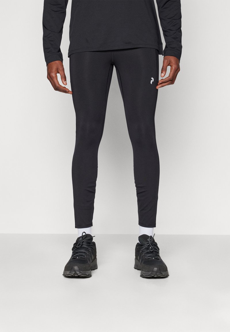 Svarta, figurnära leggings i stretchmaterial med en slät textur. Inkluderar en vit logotyp på låret och kombineras med svarta sportskor.