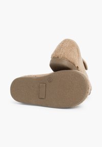 Zapatilla beige con una parte superior de textura suave y un suela de goma flexible. El tacón está ligeramente elevado, con un borde plano para mayor estabilidad.