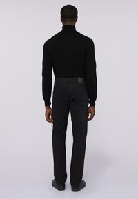 Maglione a dolce vita nero con maniche lunghe, abbinato a pantaloni scuri con una toppa in pelle sulla vita posteriore. Texture liscia.