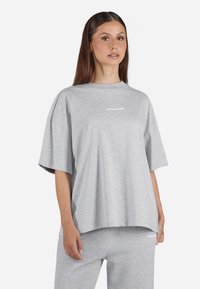 Šedé oversized tričko vyrobené z měkké bavlny, s krátkými rukávy a kulatým výstřihem, na přední straně s malým bílým logem.