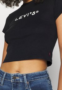 Sort cropped t-shirt lavet af bomuld med korte ærmer, der har et hvidt "LEVI'S®" logo på forsiden og en lille rød lap på siden.