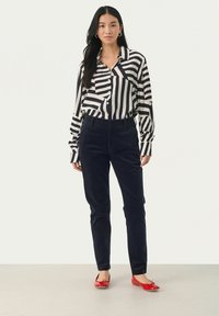 Black and white striped button-up shirt, navy corduroy pants, and red flats with bow detail. Smooth textures and tailored fit highlighted.
