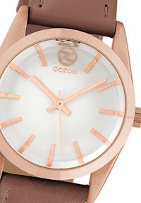 Round white dial watch with rose gold-tone markers and hands. Brown leather strap, smooth texture, and metal case with a minimalist design.